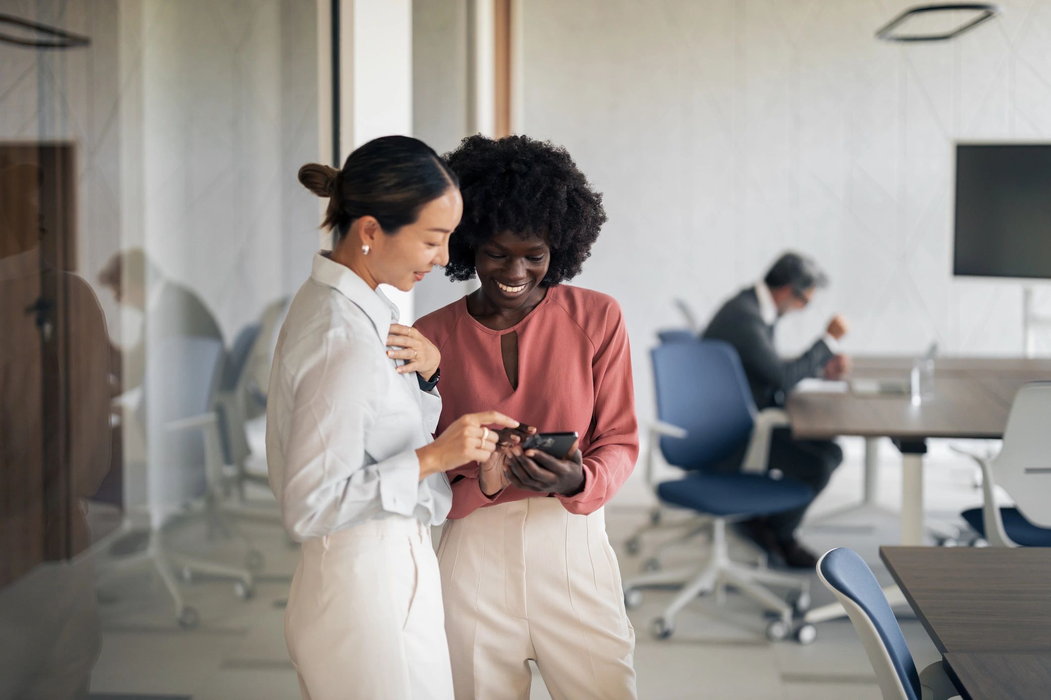 Two women reviewing something on a smartphone in an office, representing supportive mentorship